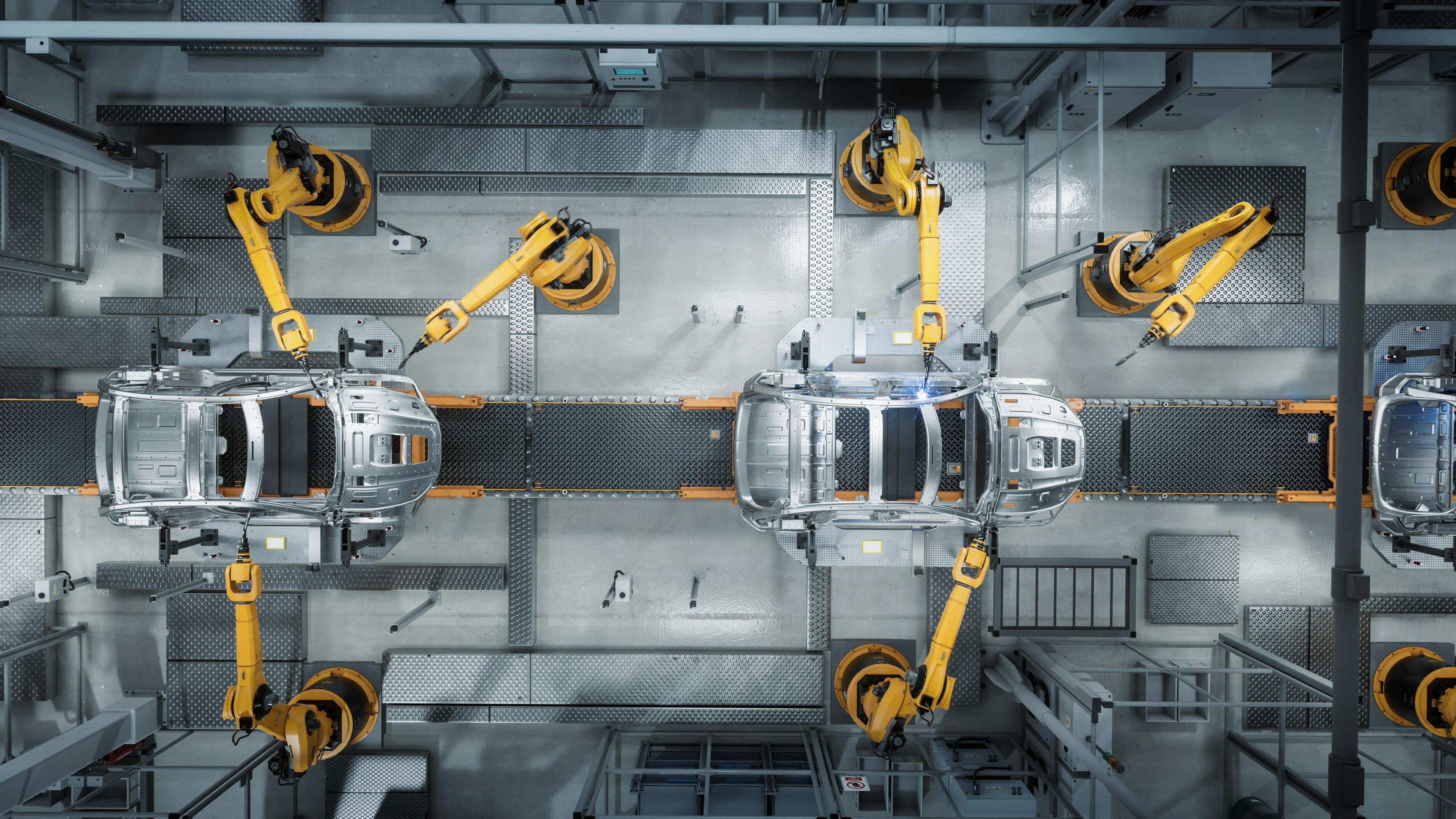 Vogelperspektive auf einen Fabrikprozess: Gelbe Roboterarme montieren zwei silberne Autos.
